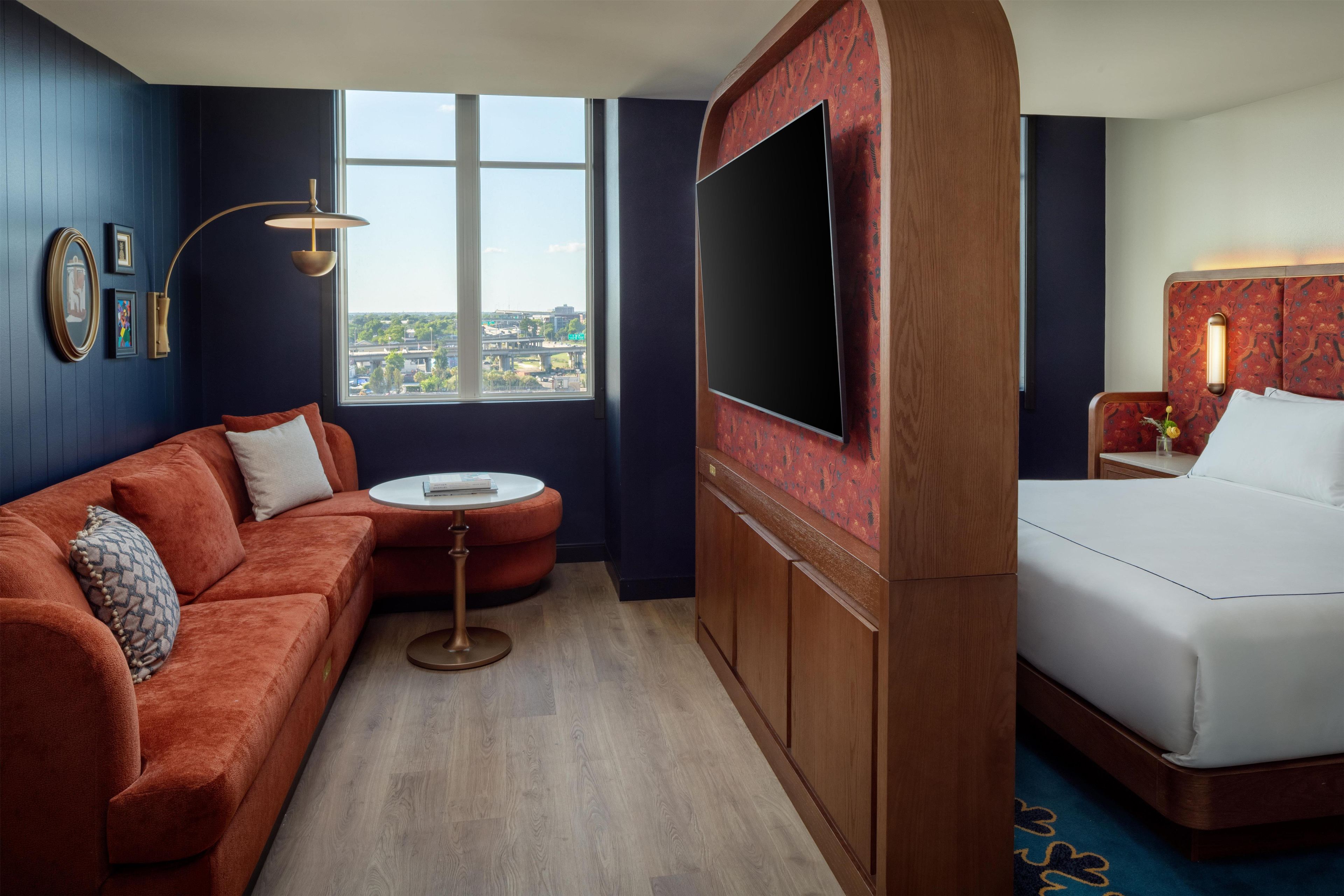 A hotel room with a large window, a sofa, a bed, a TV, and a small table.