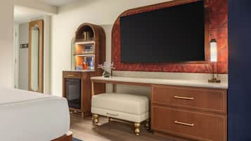Habitación de hotel con cama, escritorio con cajones, televisor, espejo y repisa con botellas.