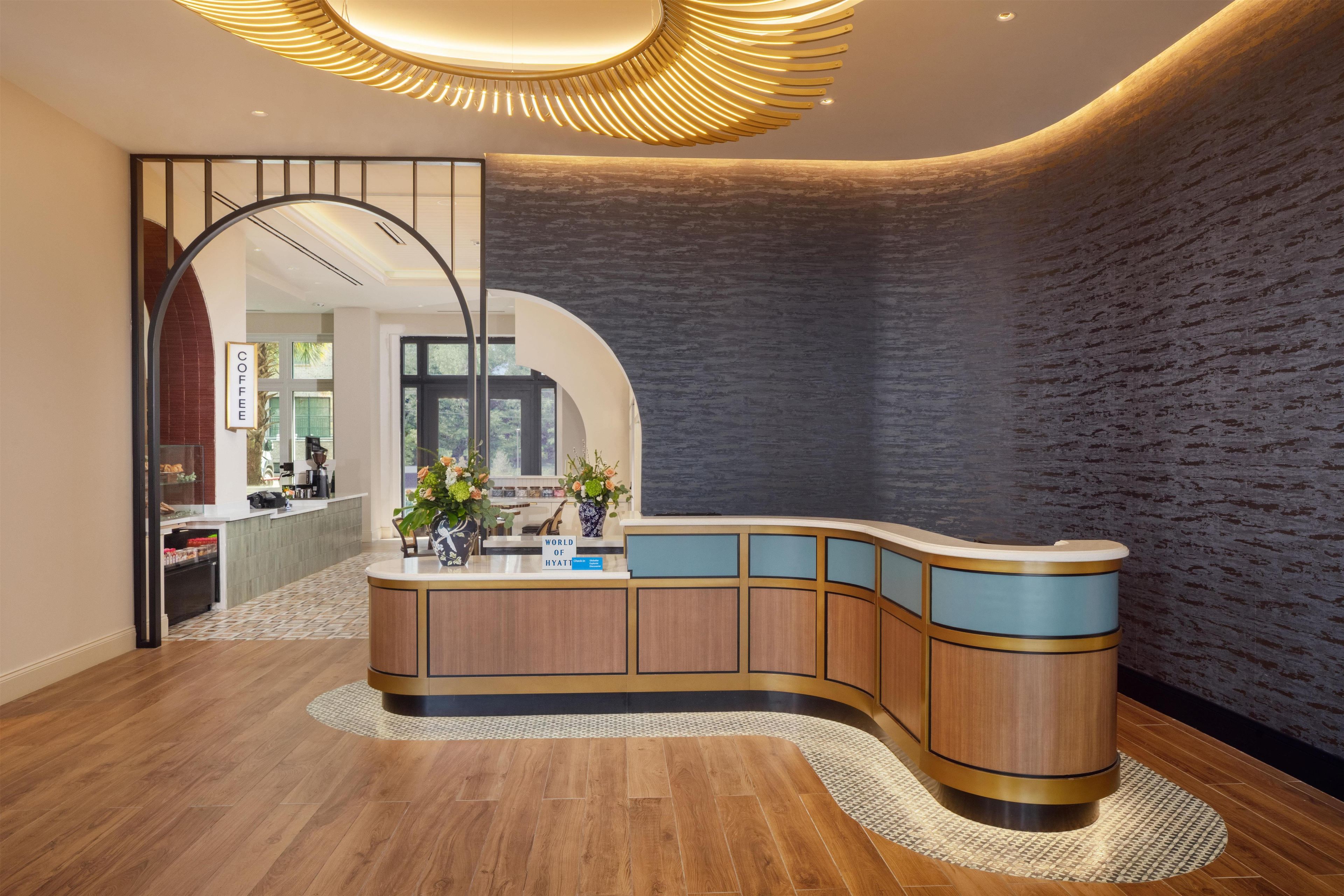 A reception area with a curved wooden counter, a modern light fixture, and a view into the adjacent room.