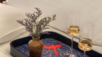 A tray with a vase of flowers and two glasses of wine on a bed with a pillow and a decorative pillowcase.