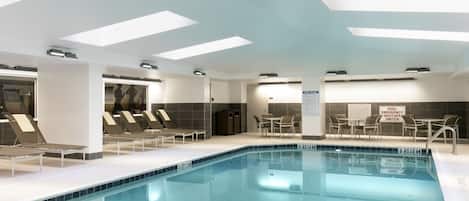 Una piscina interior moderna con agua cristalina, sillas de descanso y un interruptor de seguridad para emergencias.