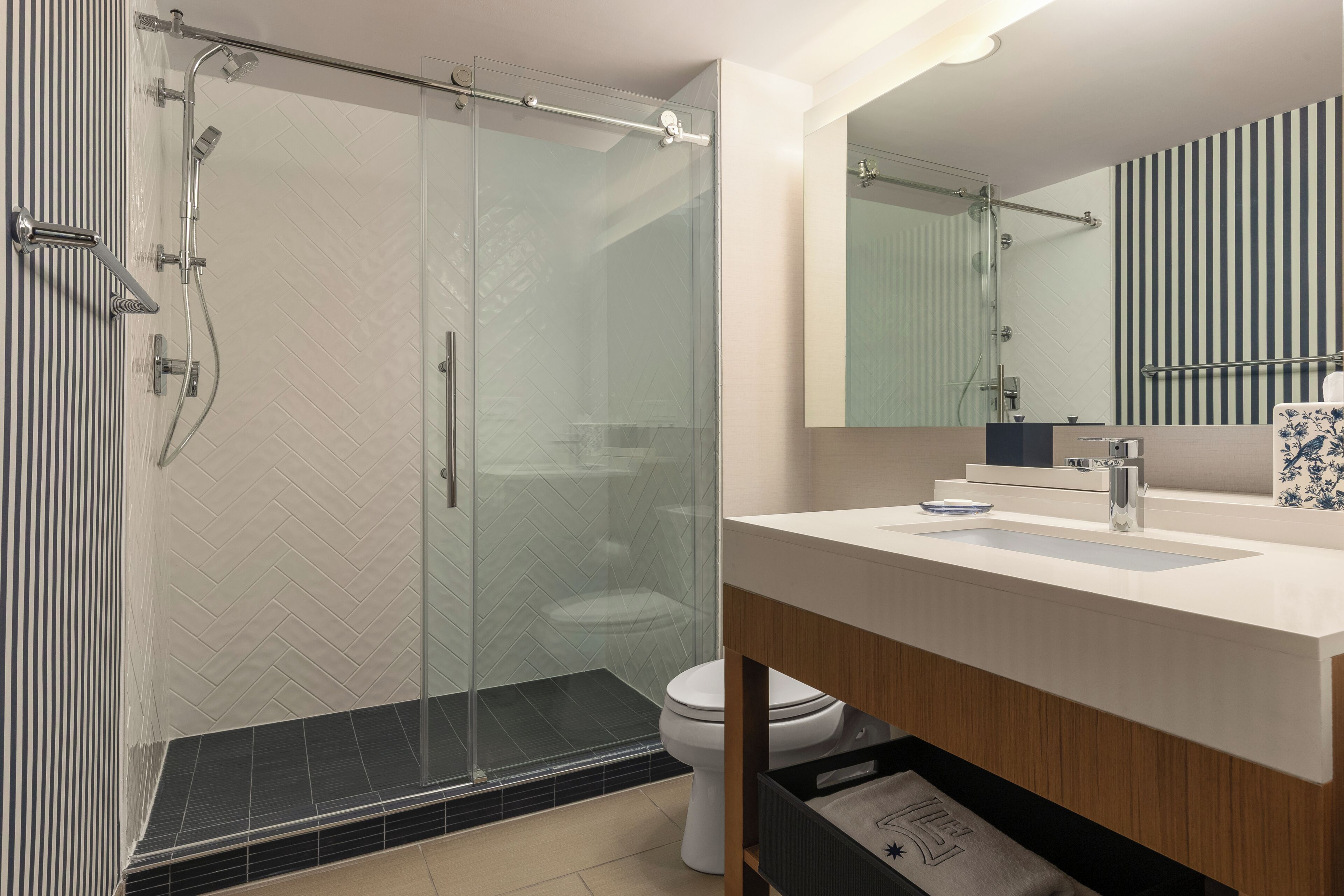 A modern bathroom with a glass-enclosed shower, a white toilet, and a wooden vanity with a mirror.