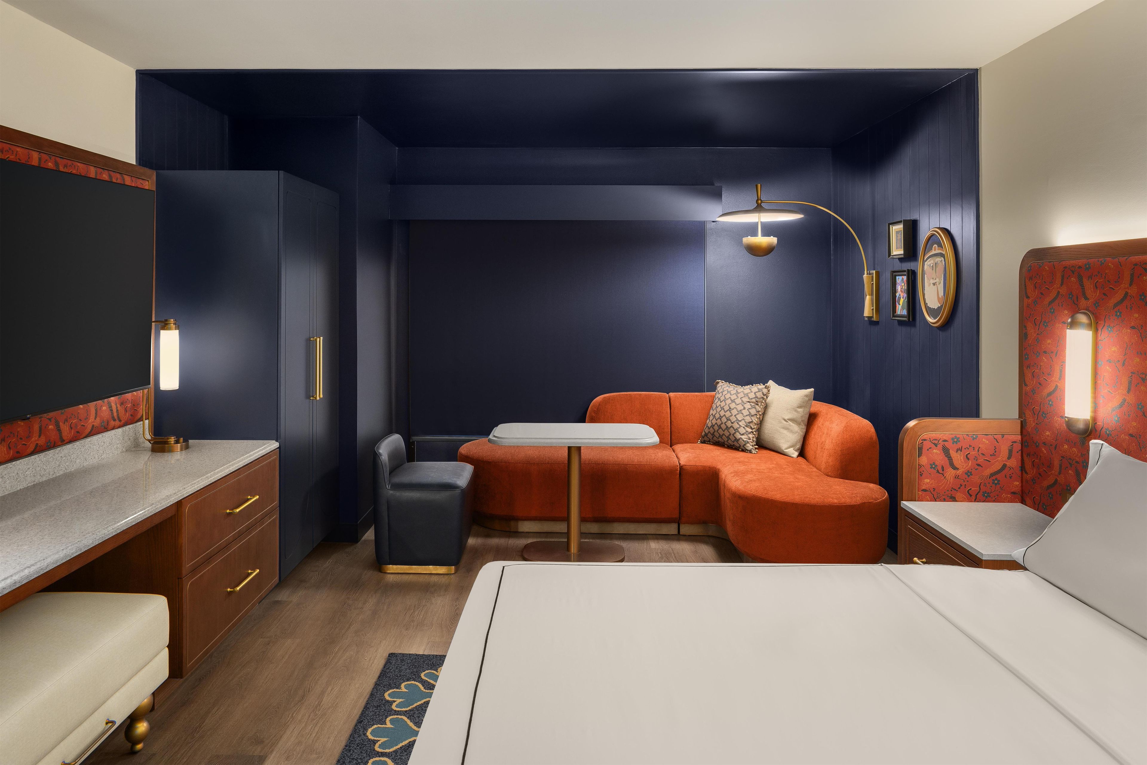 A compact hotel room with a bed, a desk, a sofa, a small table, and a chair.