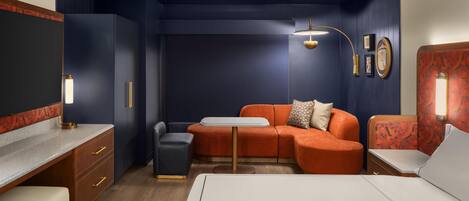 A compact hotel room with a bed, a desk, a sofa, a small table, and a chair.