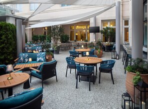 An outdoor seating area with round tables and chairs, surrounded by potted plants and a covered section with a white canopy. - The Lowline Hotel, part of JdV by Hyatt Charleston (Charleston)