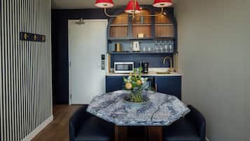 A compact kitchen with a microwave, coffee maker, and a small sink. There is a round table with a vase of flowers and two chairs.