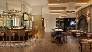 Zona de bar con una pantalla de televisión, varios taburetes y una variedad de botellas. Hay áreas de estar con mesas y sillas, y una chimenea.