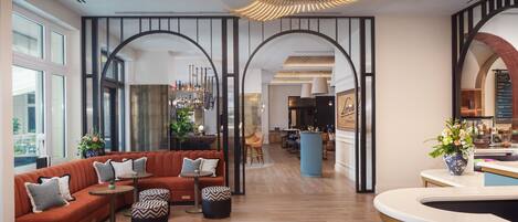 A modern hotel lobby with a red sofa, a bar area, and a view of the kitchen.