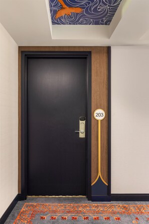 Una puerta negra con una placa de número, un panel de madera y una alfombra estampada.