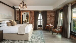 A hotel room with a large bed, a desk, a chair, a chandelier, and a view of the outdoors. - The Charmant Hotel (La Crosse)
