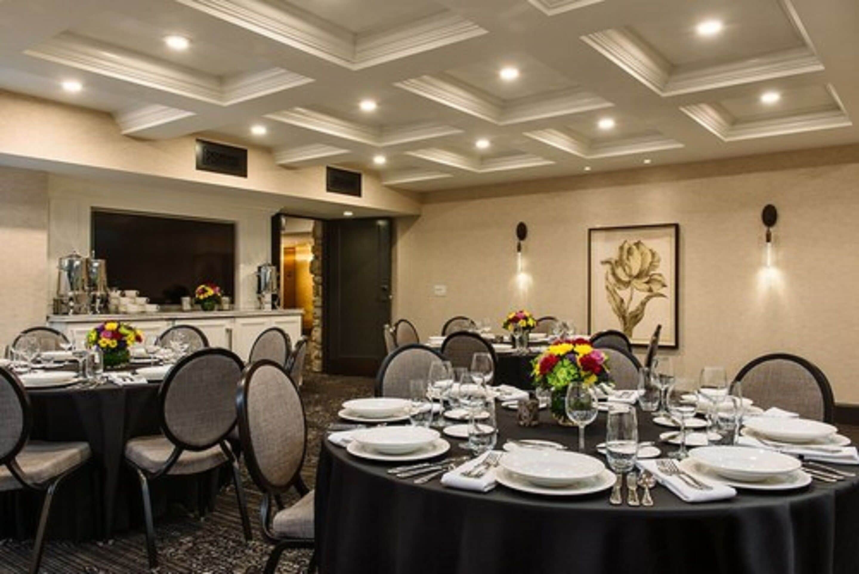 A conference room with round tables set for dining, equipped with chairs, and decorated with floral centerpieces.
