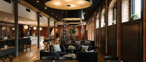 A restaurant interior with a bar area, seating with tables and chairs, and a brick wall with windows.