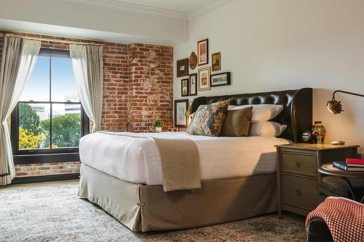 A hotel room with a large bed, a nightstand, a desk, and a window with curtains.