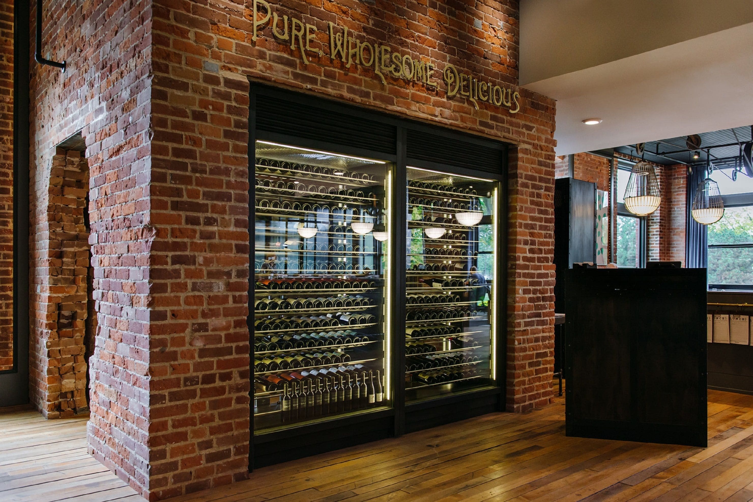 A brick wall with a wine rack and a sign that reads "PURE WHOLESALE DELICIOUS."
