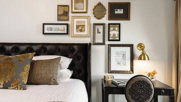 Un dormitorio ordenado con un cabecero capitonado, una mesita de noche con lámpara, y una silla con respaldo decorativo.
