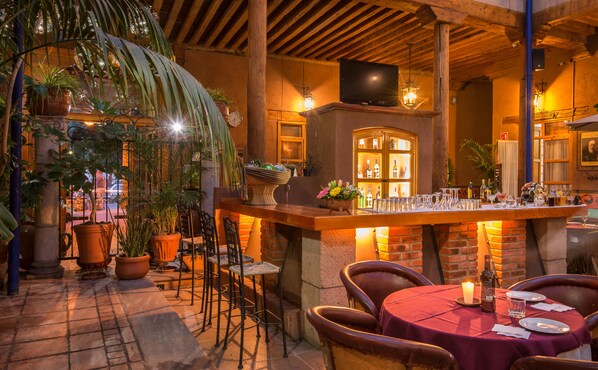 An outdoor patio area with brick walls, wooden beams, and potted plants.