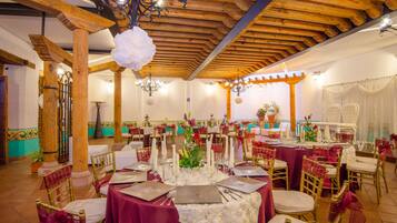A banquet hall with round tables set for dining, wooden beams on the ceiling, and a chandelier.