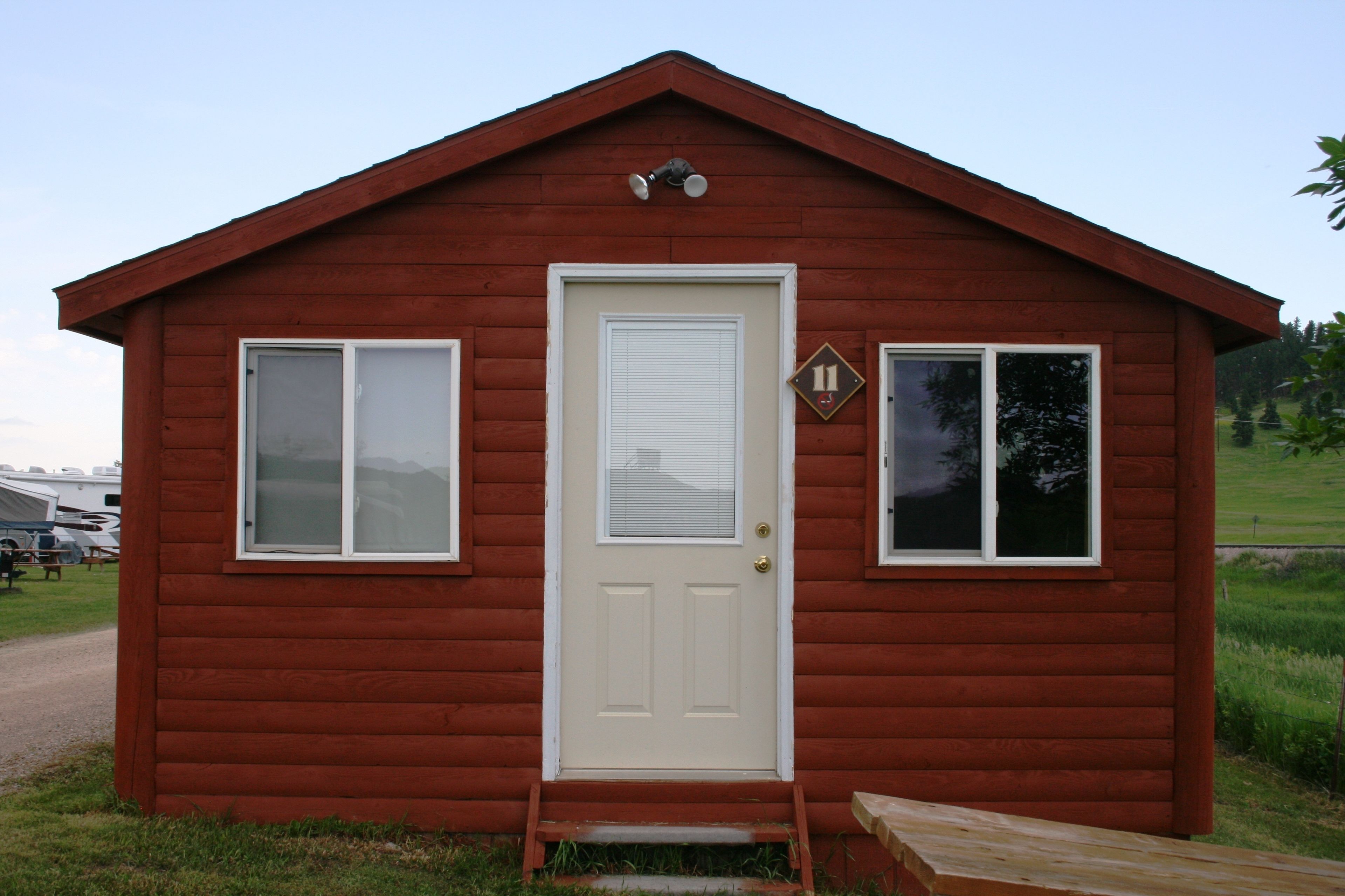 A small, single-story wooden cabin with a white door and two windows, a small porch, and a visible number '11' sign.