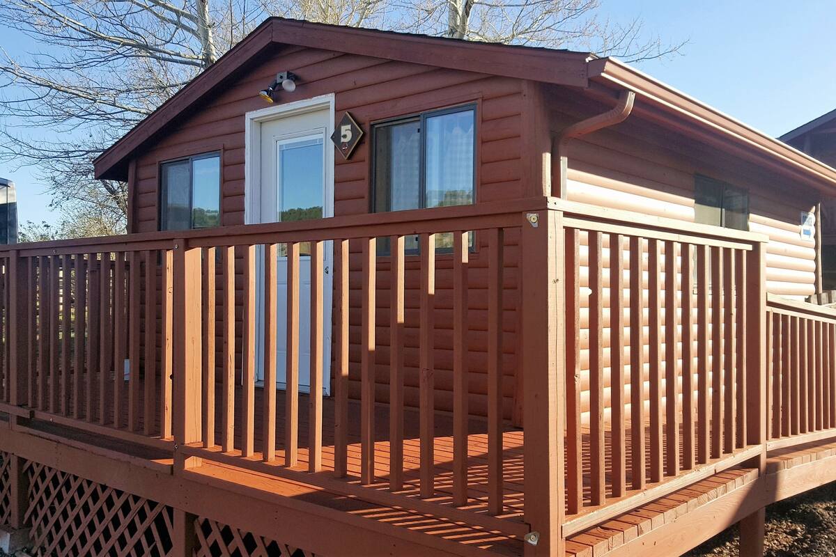 A wooden cabin with a deck, a front door, and a window.