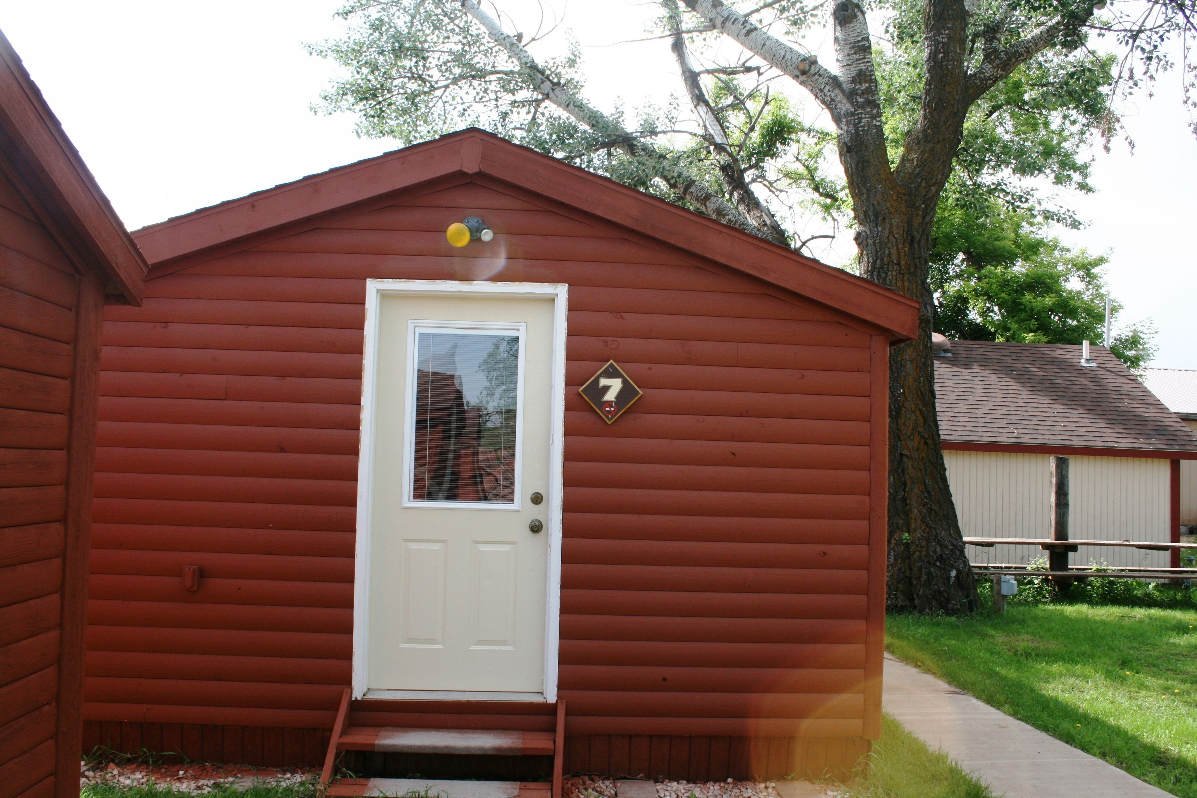 A small, single-story wooden cabin with a white door and a number '7' sign on the wall.