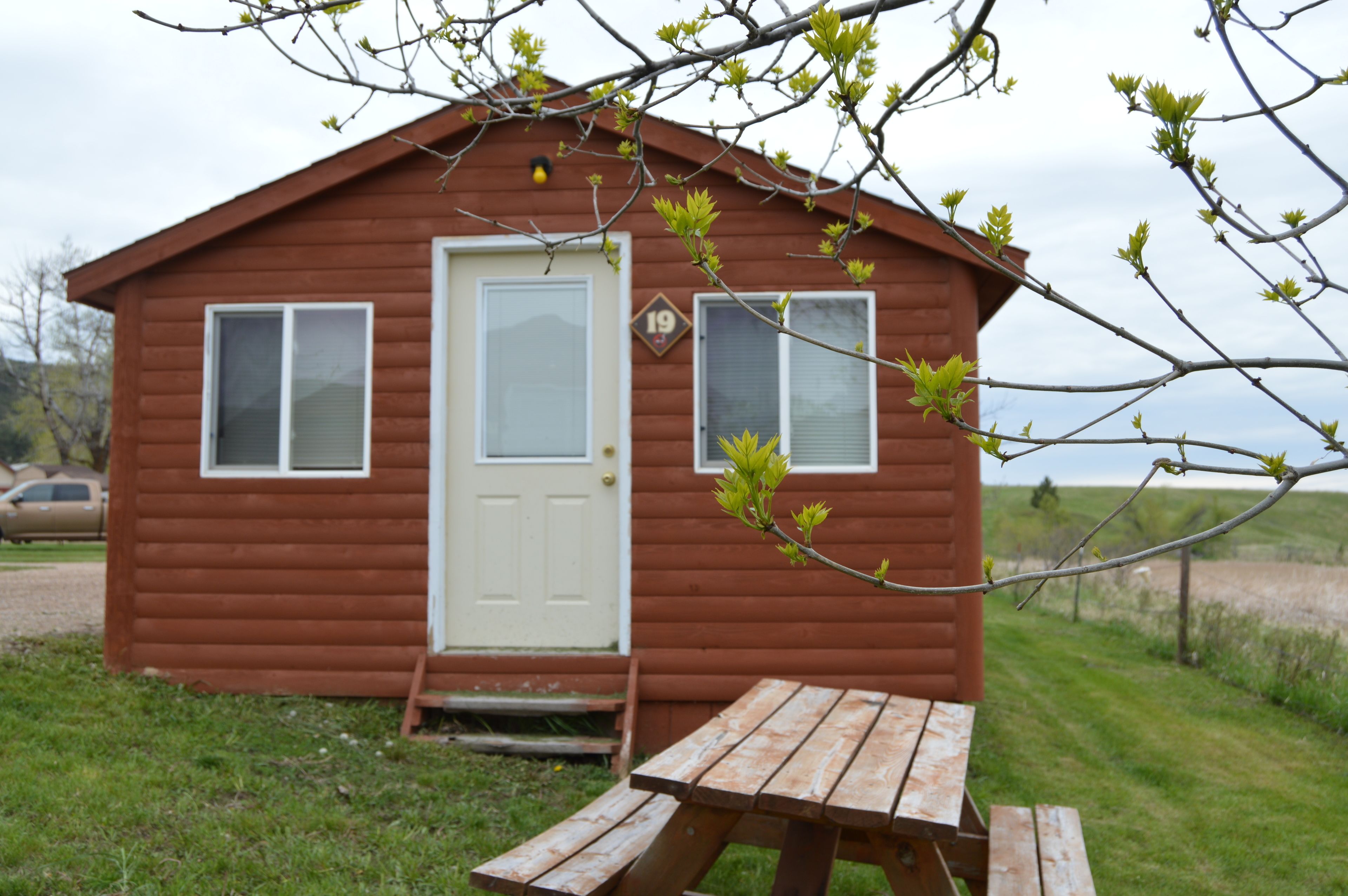 Una cabaña de madera pequeña con una puerta blanca, dos ventanas y un cartel con el número 19.