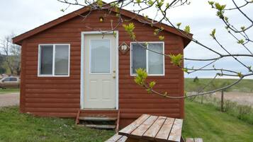 Una cabaña de madera pequeña con una puerta blanca, dos ventanas y un cartel con el número 19.