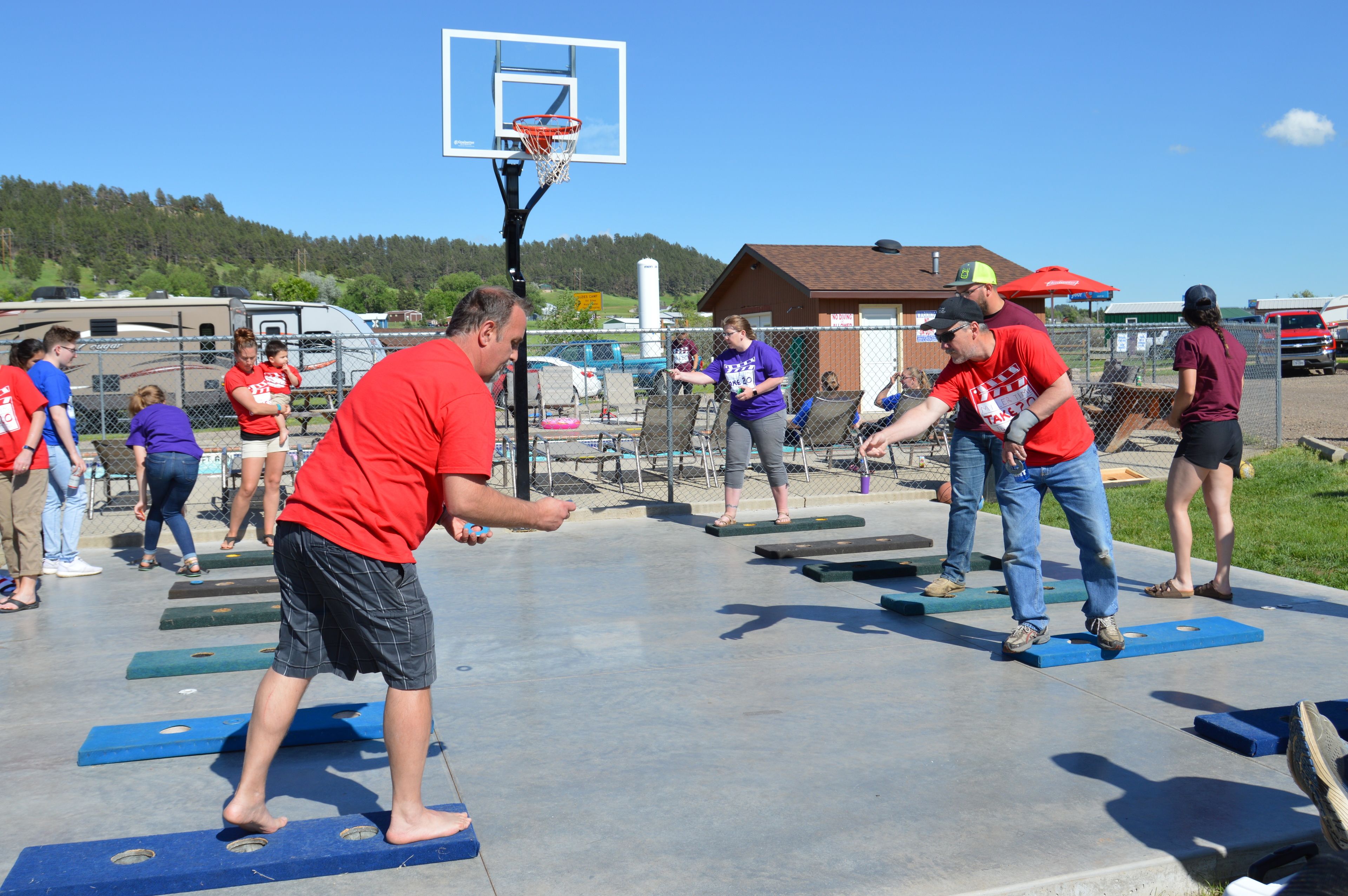 An outdoor basketball court with a hoop, surrounded by people playing.