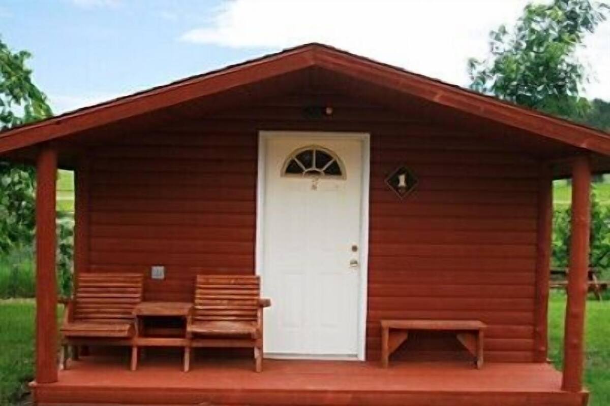 A wooden cabin with a white door, two wooden benches, and a small porch.