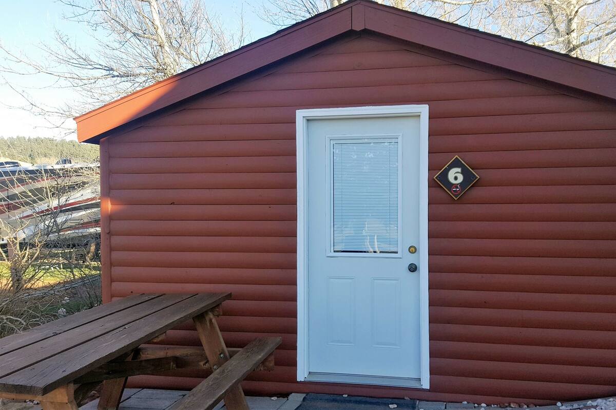 A red wooden shed with a white door, a number '6' sign, and a picnic table in front.