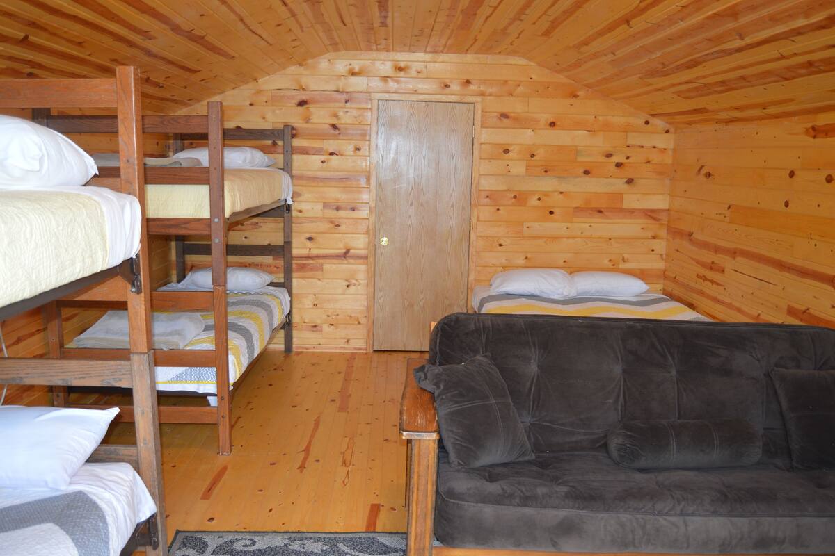 A wooden cabin room with bunk beds, a couch, and a door.