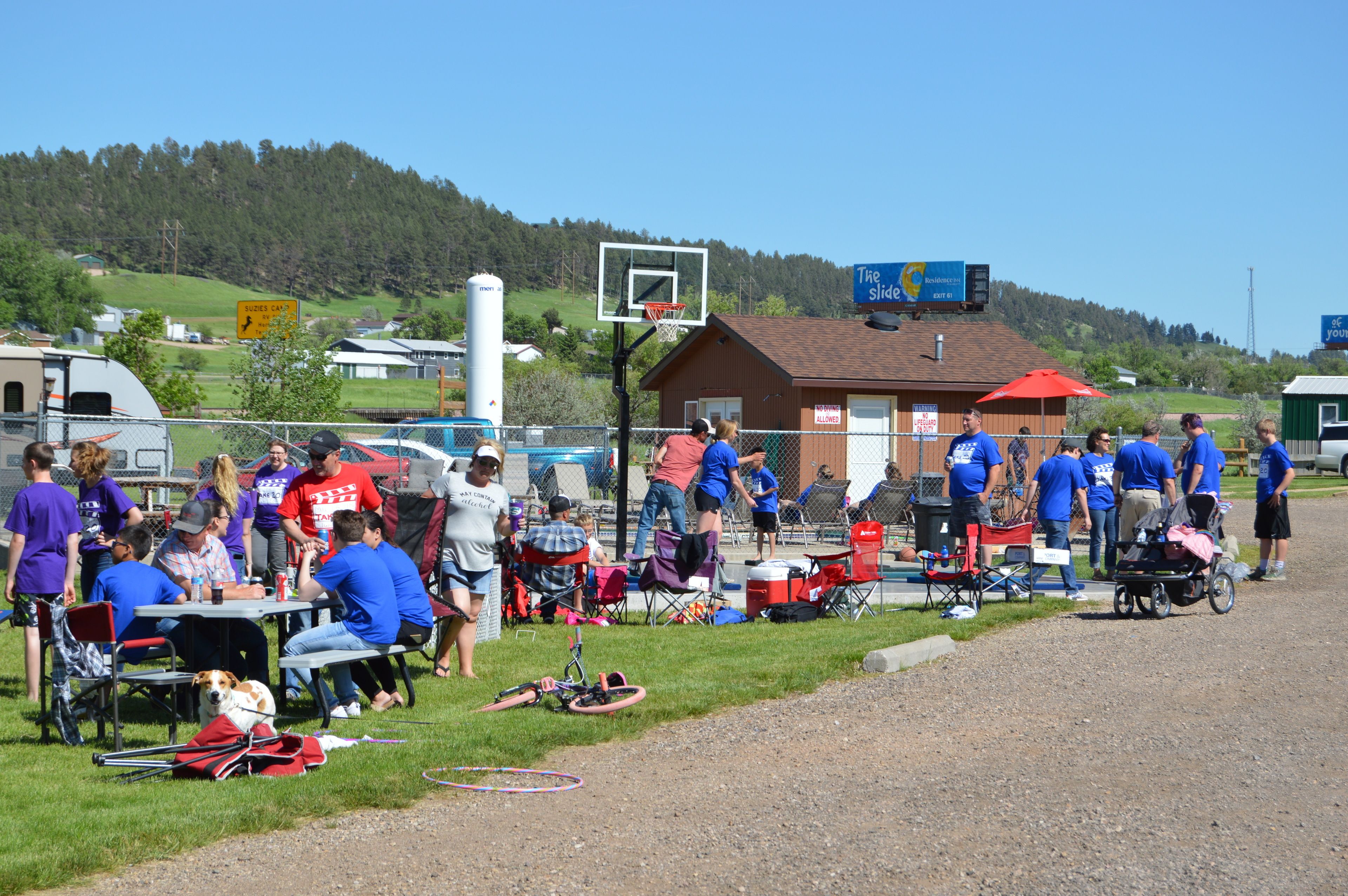 Une réunion en plein air avec des personnes, un panier de basket et un bâtiment en arrière-plan.
