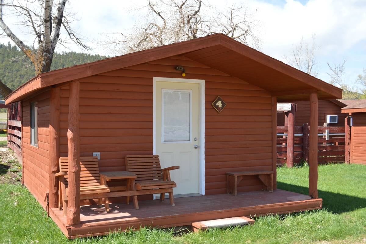 A wooden cabin with a porch, a door, and a small sign indicating the number 4.