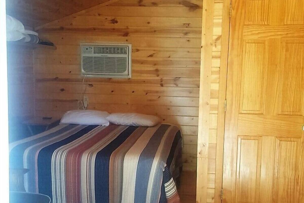 A wooden cabin room with a bed, a door, and a ceiling fan.