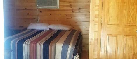 Une pièce de style cabane en bois, avec un lit, une porte et un ventilateur de plafond.