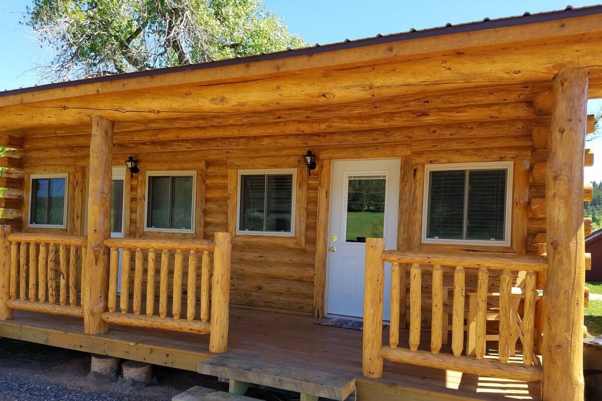 A wooden cabin with a porch, a door, and windows.
