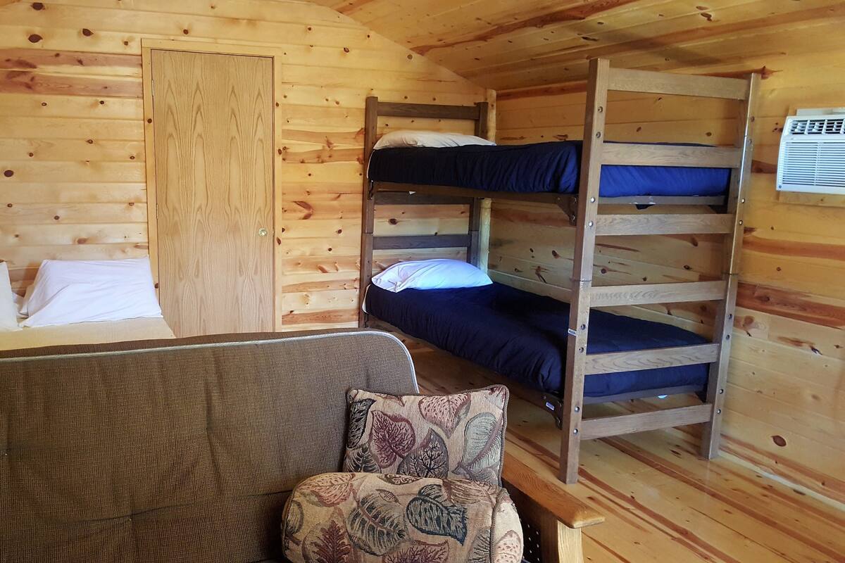 A wooden cabin room with bunk beds, a sofa, and a patterned cushion.