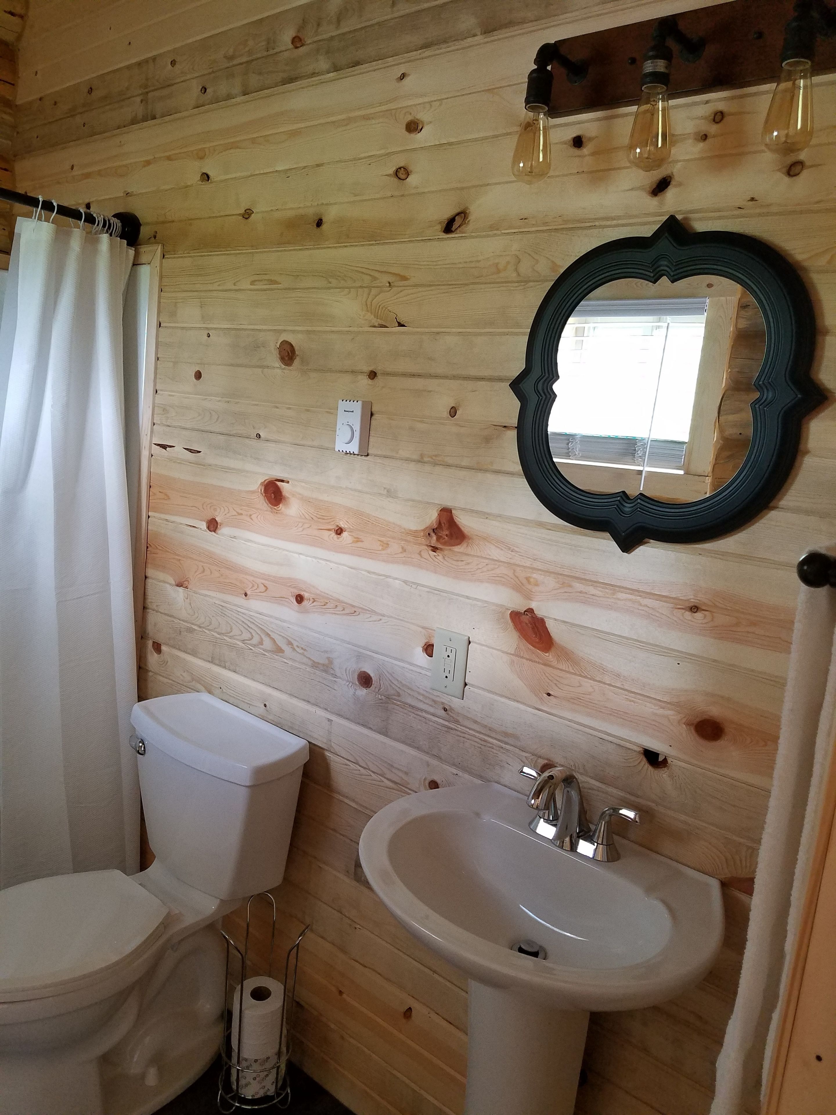 Et badeværelse med træpaneler, toilet, vask og spejl.