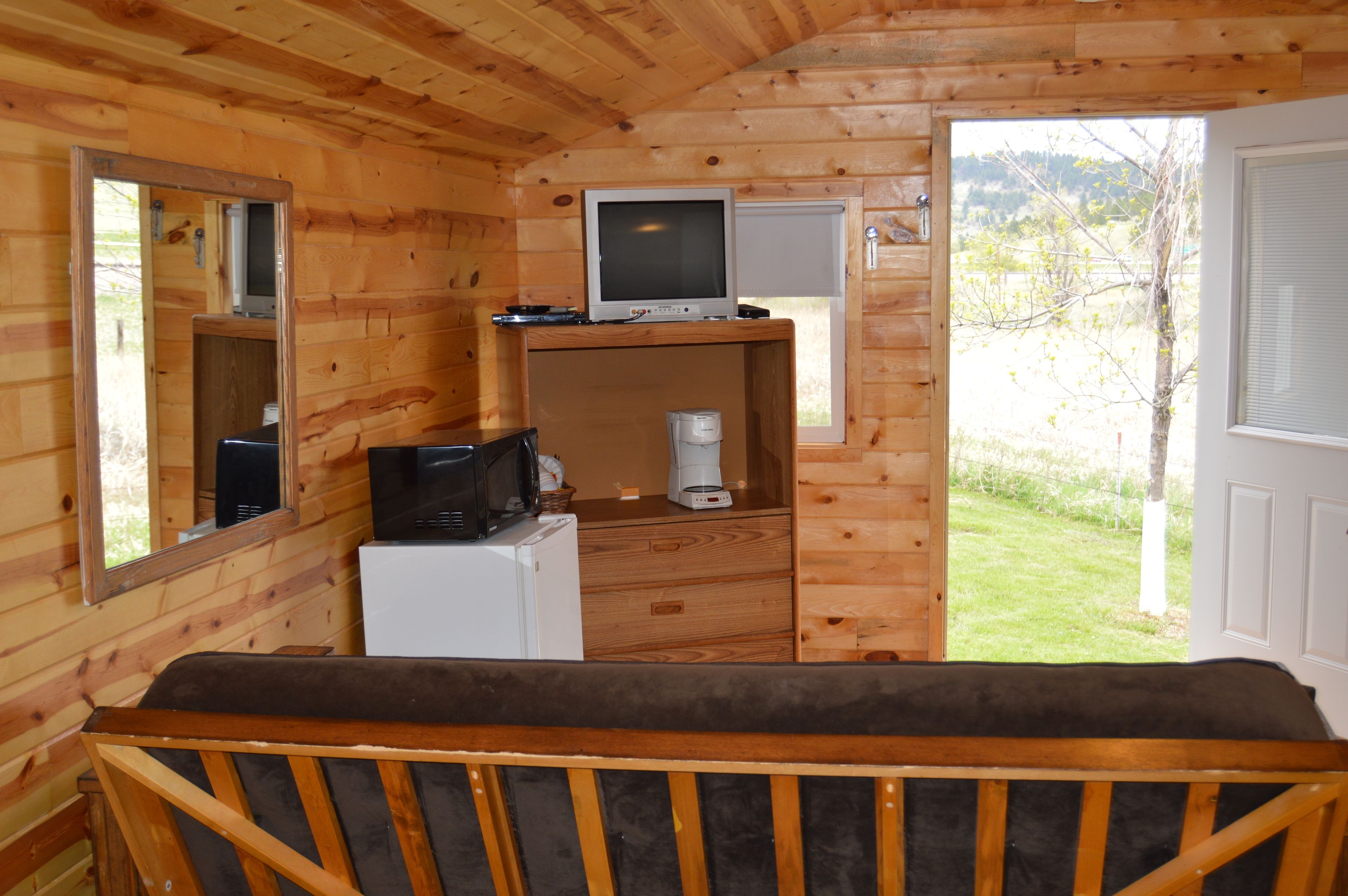 A wooden cabin room with a bed, a television, a microwave, and a refrigerator.