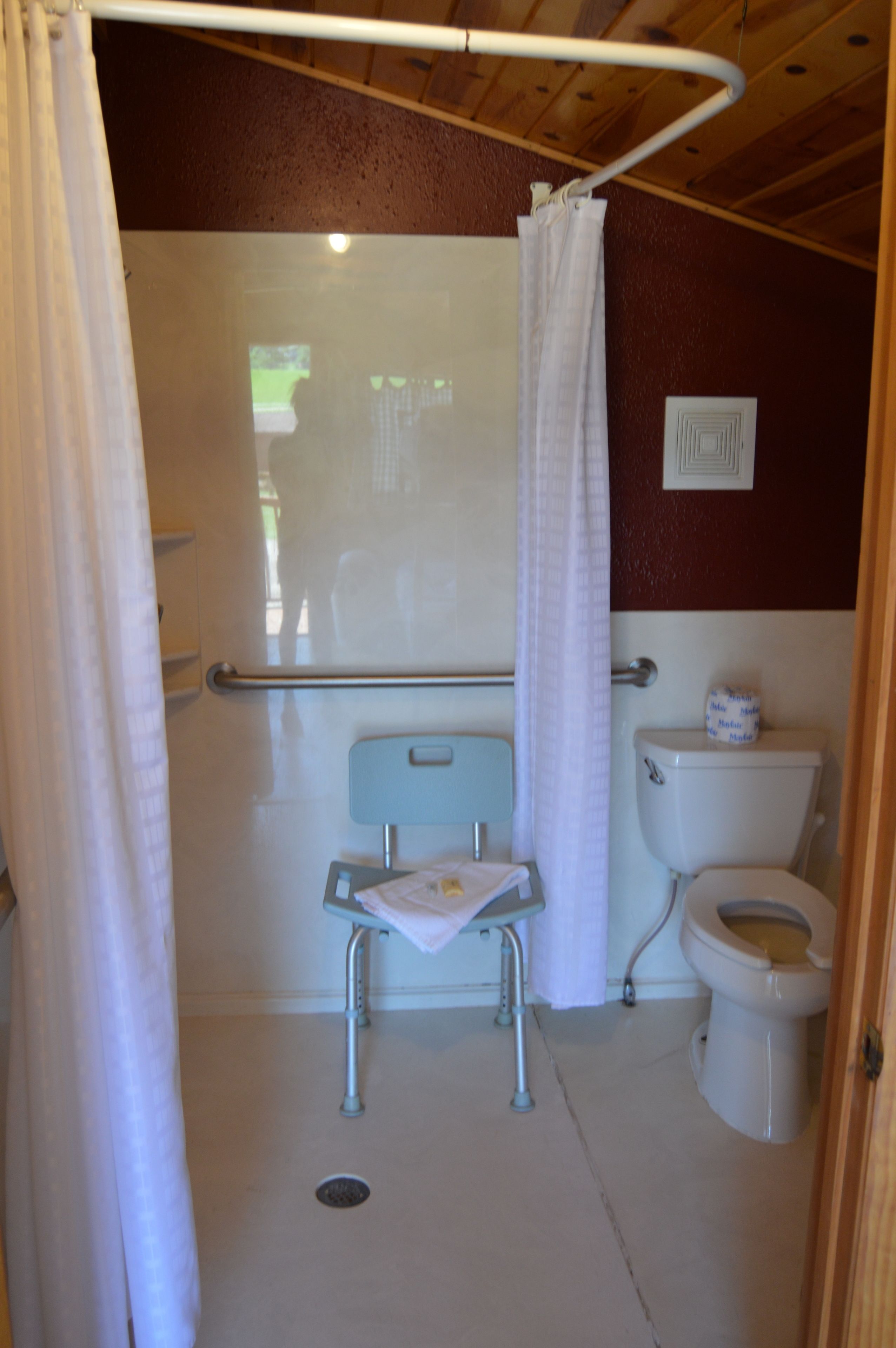Ein kleines Badezimmer für Einzelpersonen mit Dusche, Toilette und einer rollstuhlgerechten Sitzbank.