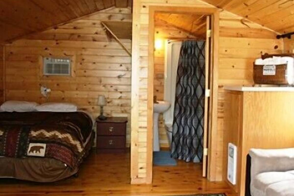 A log cabin bedroom with a bed, dresser, and a small window.