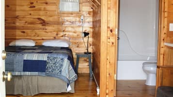 Una habitación de cabaña de madera con una cama, una mesita pequeña, un calentador y un baño.