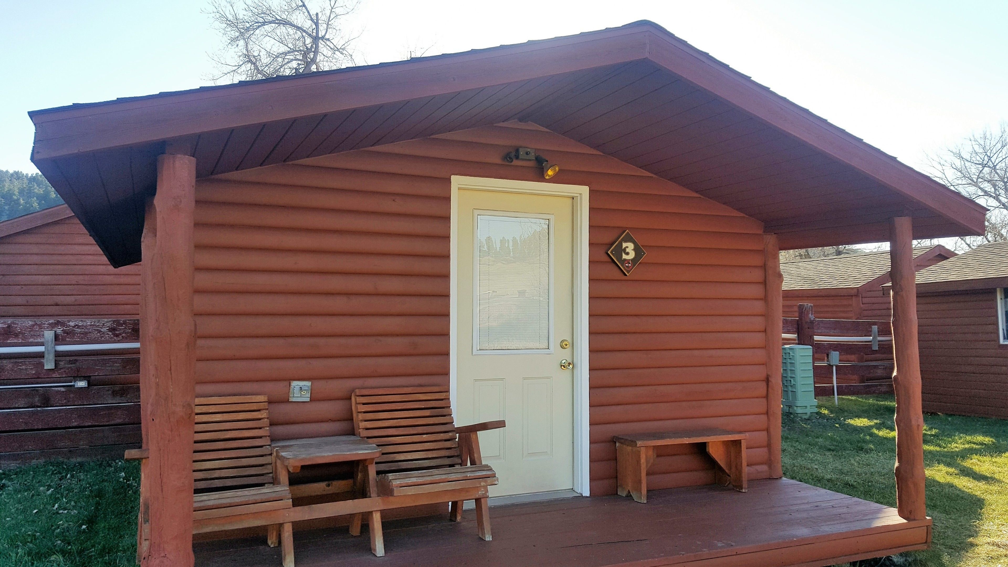 A wooden cabin with a porch, a door, and a bench.