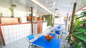 A restaurant with blue tables and chairs, a kitchen area, and potted plants. - Hotel Flor Blanca (Quepos)