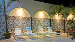 A poolside area with lounge chairs and a stone wall. - Hotel Flor Blanca (Quepos)