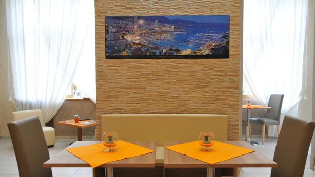A dining area with a wooden table and chairs, a painting of a coastal cityscape, and a stone wall. - Hotel Montecarlo (Milan)