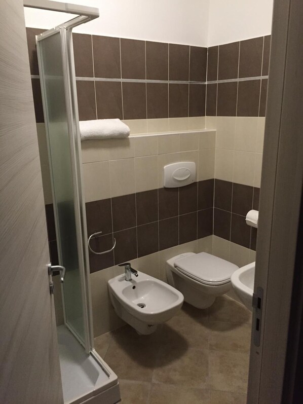 A bathroom with a glass shower enclosure, a bidet, a toilet, and a sink.