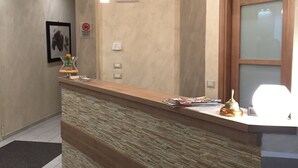 A reception desk with a clock, pendant lights, and a framed picture on the wall. - Hotel Montecarlo (Milan)