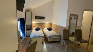 A hotel room with two single beds, a desk with a chair, a TV mounted on the wall, and a mirror on the door. - Hotel Montecarlo (Milan)