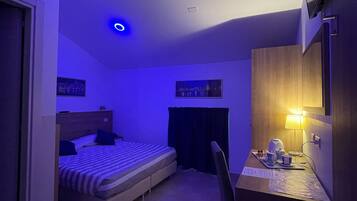 A bedroom with a bed, a desk with a chair, a television, and a lamp.