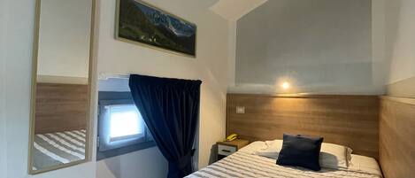 A bedroom with a bed, a nightstand, a mirror, a window with curtains, and a painting on the wall.